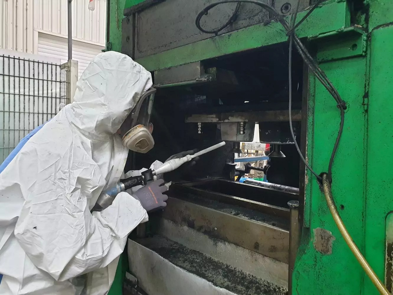 Ile kosztuje czyszczenie suchym lodem? 1 Osoba w odzieży ochronnej i masce oddechowej używa narzędzia do czyszczenia lub naprawy maszyn wewnątrz dużej maszyny przemysłowej, demonstrując proces i wydajność Ile Kosztuje Czyszczenie Suchym Lodem.