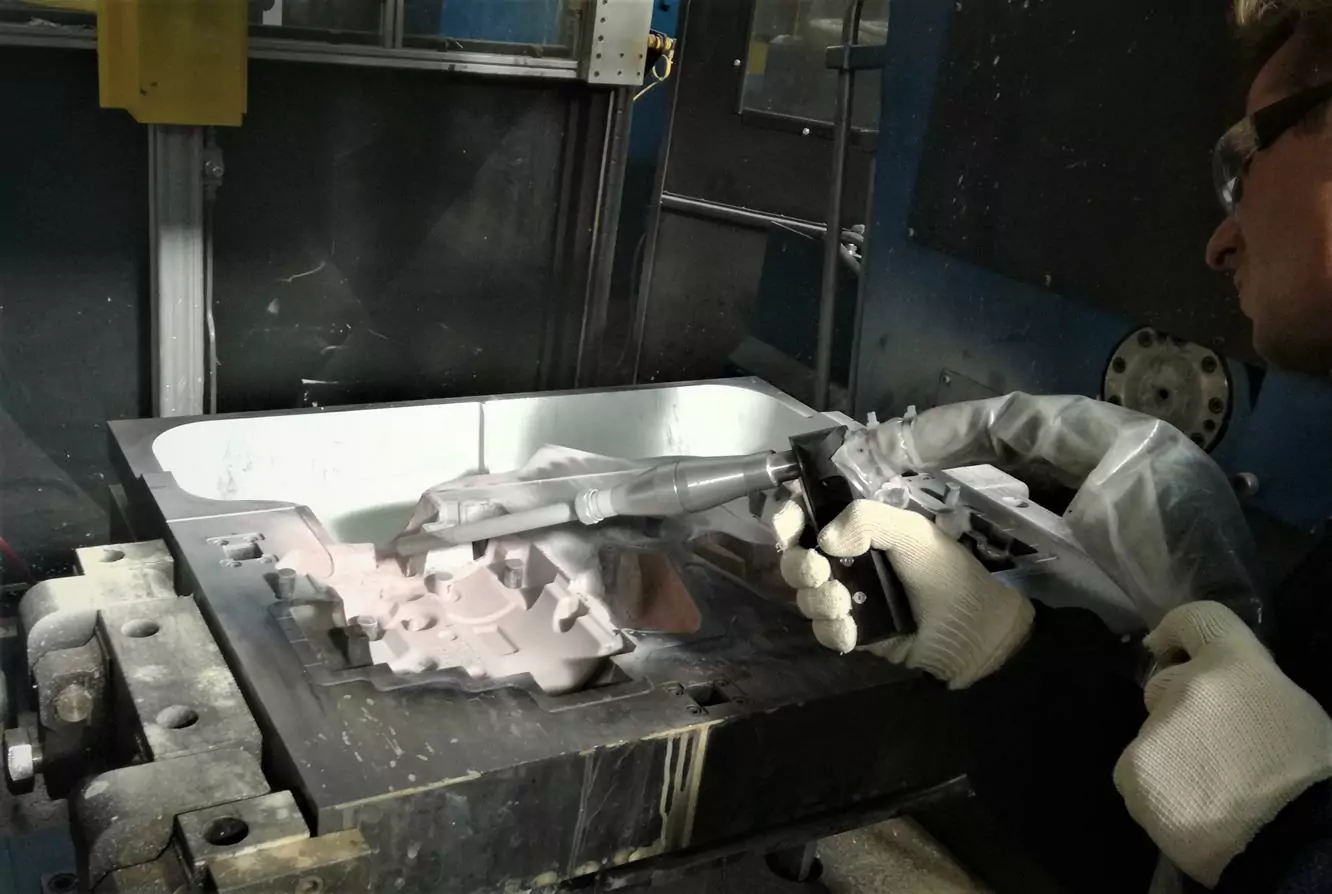 Przemysł odlewniczy 4 Osoba w białych rękawiczkach i okularach ochronnych używa pistoletu natryskowego do pokrycia formy białą substancją w warsztacie przemysłowym, demonstrując Czyszczenie Form Odlewniczych Suchym Lodem na metalowym stole.