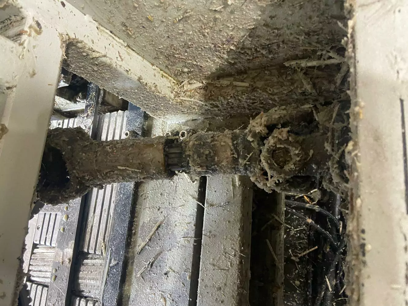 Przemysł drzewny 6 Zbliżenie brudnej, skorodowanej rury lub części mechanicznej pokrytej kurzem i brudem, podkreślające potrzebę Czyszczenia Maszyn Stolarskich Suchym Lodem w warunkach warsztatu przemysłowego z metalowymi powierzchniami i rozrzuconymi odpadkami.