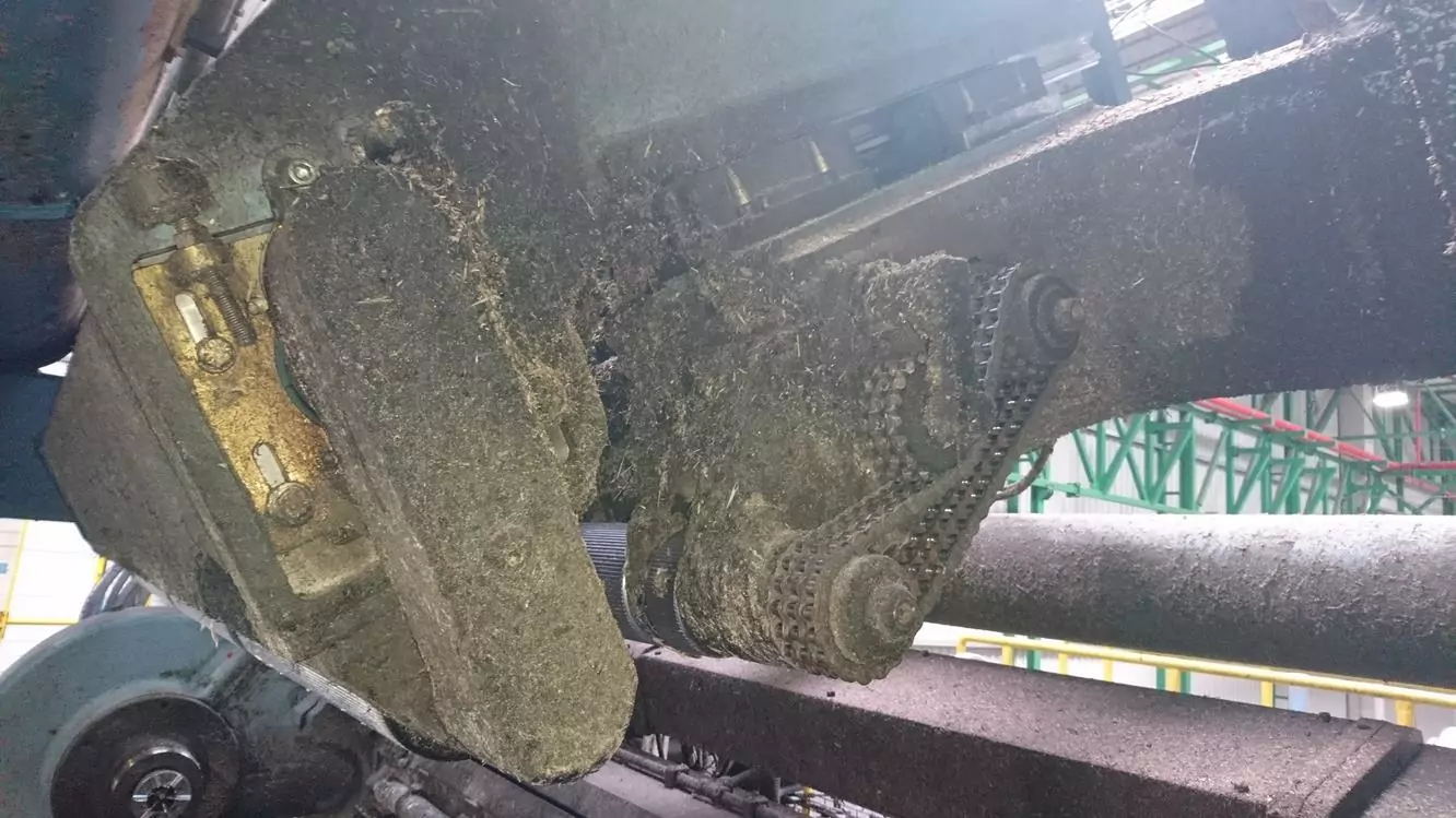 Przemysł drzewny 2 Widok z bliska zakurzonego i zatłuszczonego przemysłowego mechanizmu napędu łańcuchowego, w tym kół zębatych i elementów metalowych, wewnątrz fabryki. Obraz podkreśla obszary, w których Czyszczenie Maszyn Stolarskich Suchym Lodem może przywrócić czystość i wydajność.