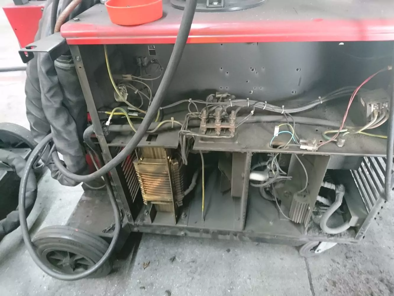 Czyszczenie spawalni i spawarek 6 Zbliżenie na otwartą maszynę z odsłoniętym okablowaniem, metalowymi komponentami i płytkami drukowanymi wewnątrz metalowej obudowy. Prezentowana w Galerii Zdjęć Czyszczenia Suchym Lodem, jest osadzona w industrialnym otoczeniu z czarnymi kablami i czerwonym pojemnikiem na górze.