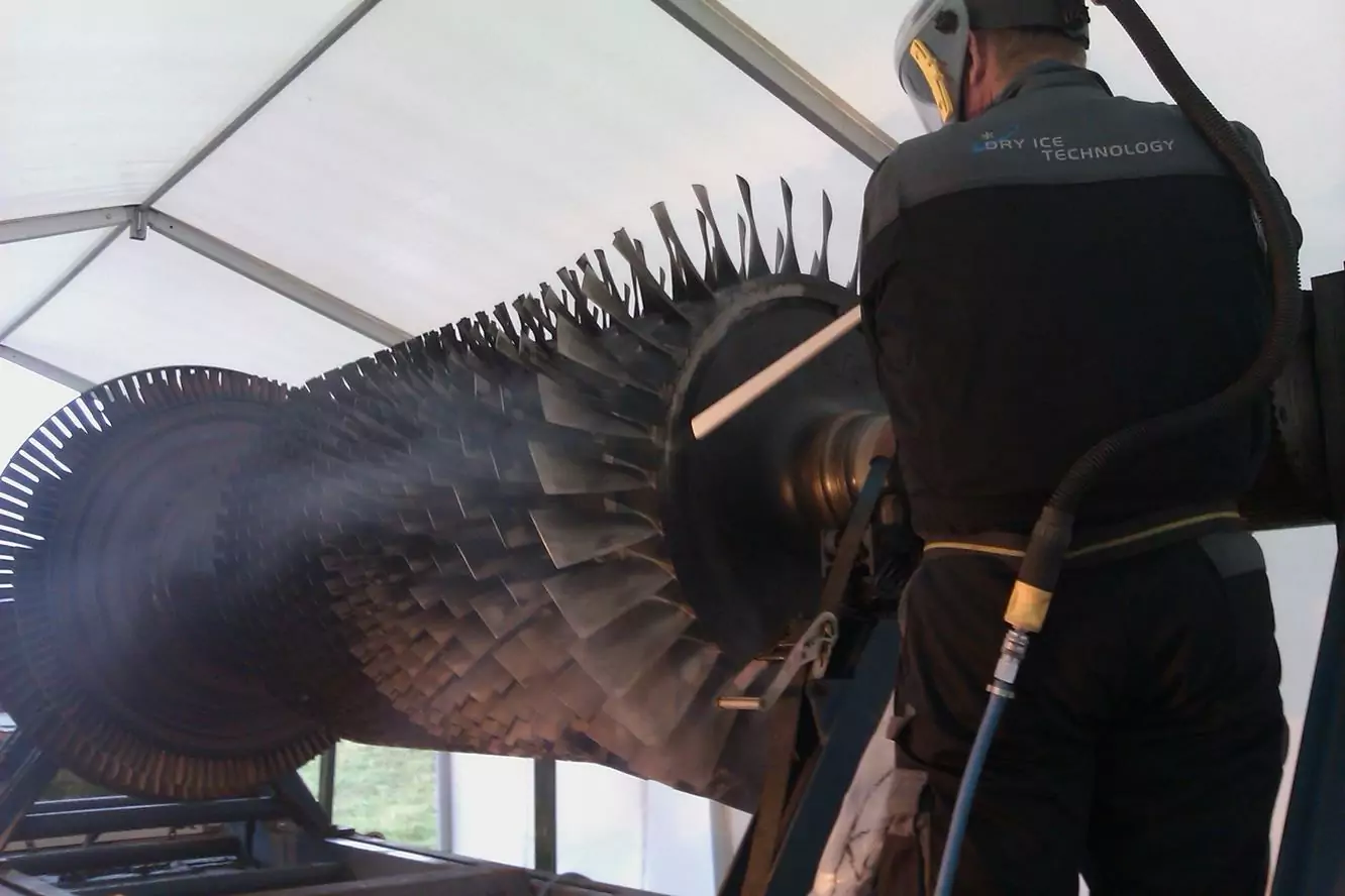 Czyszczenie instalacji i urządzeń elektrycznych 4 Pracownik w odzieży ochronnej używa sprzętu do czyszczenia suchym lodem dla Czyszczenia Rozdzielni Elektrycznych Suchym Lodem, czyszcząc łopatki dużej turbiny przemysłowej wewnątrz zadaszonego miejsca pracy.