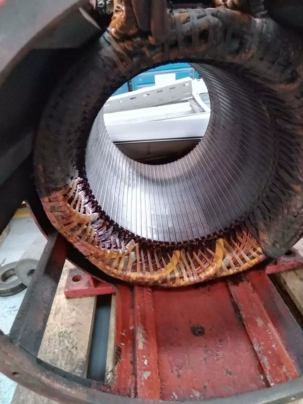 Czyszczenie instalacji i urządzeń elektrycznych 12 Zbliżenie wnętrza stojana silnika elektrycznego przedstawiające miedziane uzwojenia i metalowy rdzeń, umieszczone na czerwonej metalowej podstawie w warsztacie, w którym przeprowadza się Czyszczenie Rozdzielni Elektrycznych Suchym Lodem w celu zapewnienia optymalnej czystości.