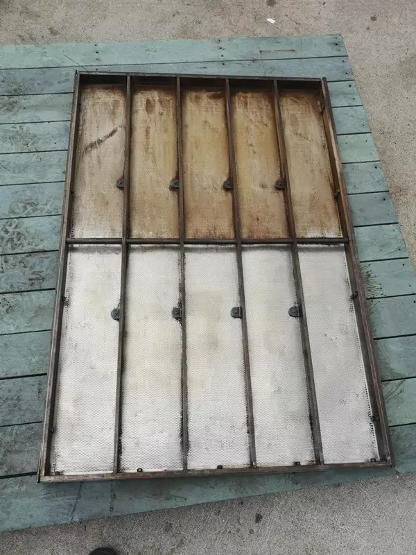 Przemysł spożywczy 4 Prostokątna metalowa rama z sześcioma pionowymi sekcjami - trzema rdzawobrązowymi, trzema srebrnymi i czystymi - leżąca na zwietrzałej niebieskiej drewnianej powierzchni, ukazująca efekty Czyszczenia Maszyn Spożywczych Suchym Lodem.