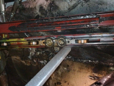 Zbliżenie na metalowy system szynowy z rolkami i kołami zębatymi na czerwonej ramie. Srebrny pręt jest regulowany, a ciemne, tłuste powierzchnie wskazują na konserwację - idealne do demonstracji Filmy z Czyszczenia Suchym Lodem.